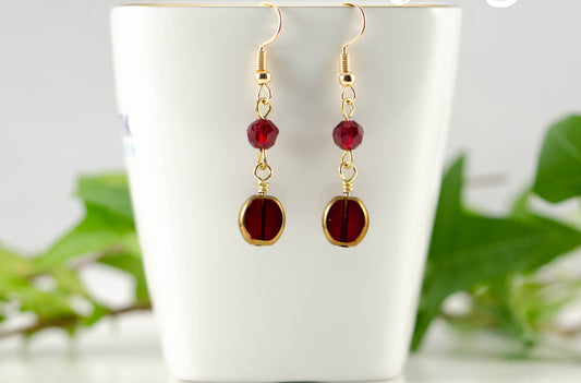 Dark Red and Gold Glass Bead Earrings displayed on a tea cup.