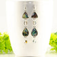 Long Abalone Shell and Glass Crystal Earrings displayed on a coffee mug.
