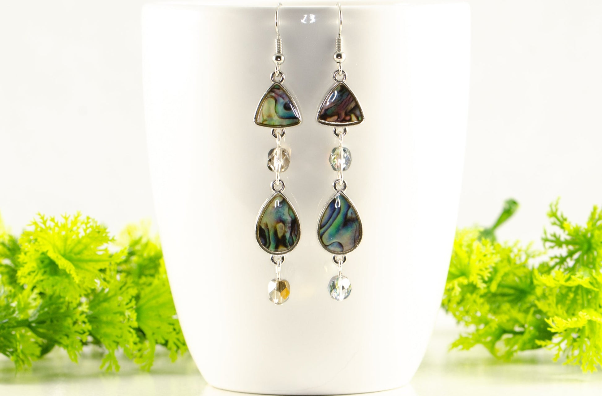 Long Abalone Shell and Glass Crystal Earrings displayed on a coffee mug.