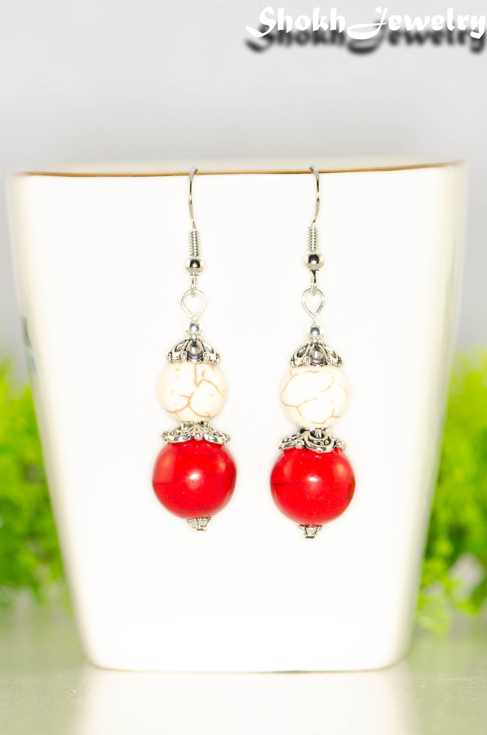 Red and White Howlite Dangle Earrings displayed on a tea cup.