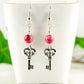 Red Quartzite and Key Charm Dangle Earrings displayed on a tea cup.