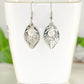 Filigree Silver Leaf Charm and Clear Glass Crystal Earrings displayed on a tea cup.