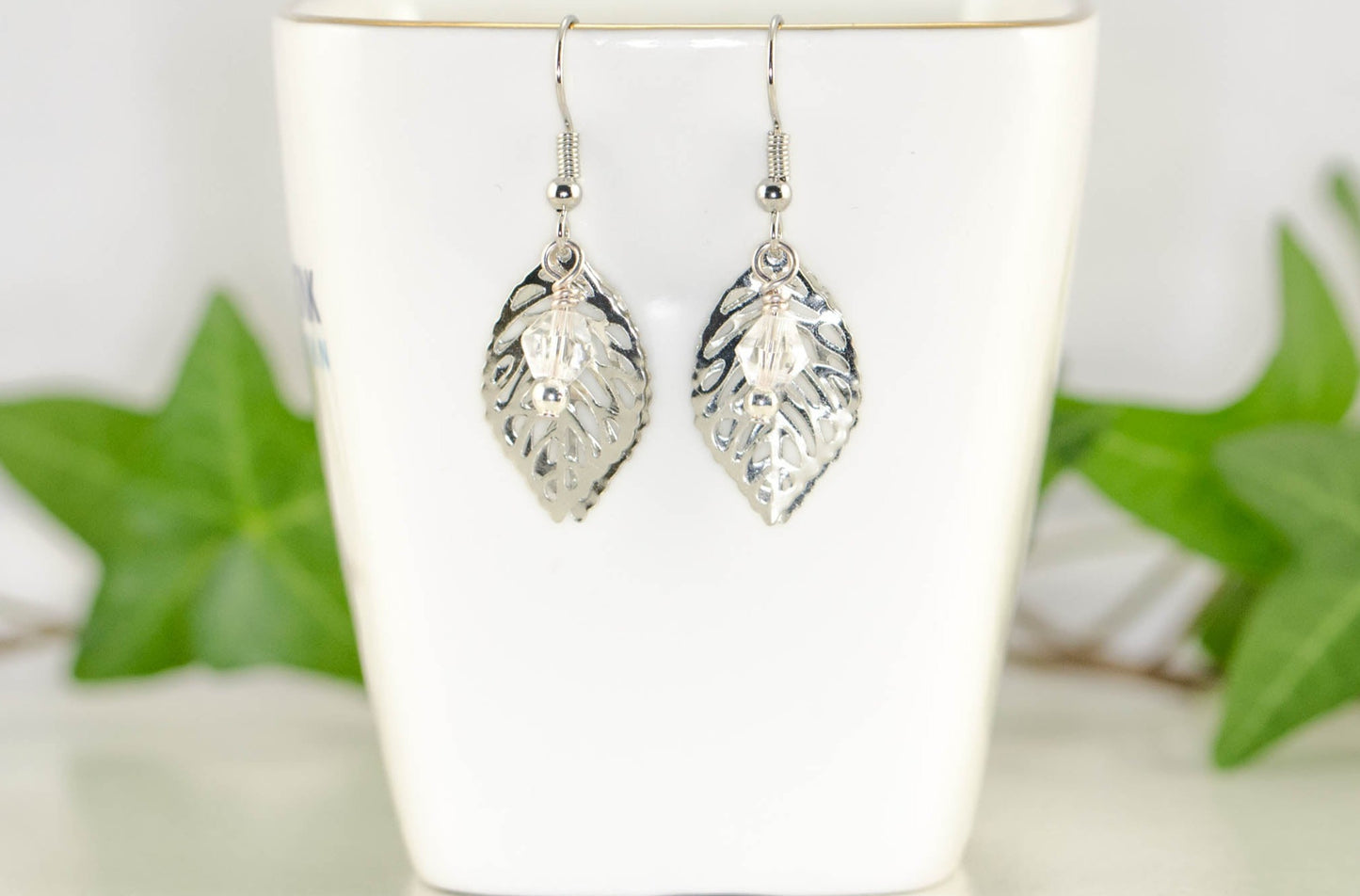 Filigree Silver Leaf Charm and Clear Glass Crystal Earrings displayed on a tea cup.