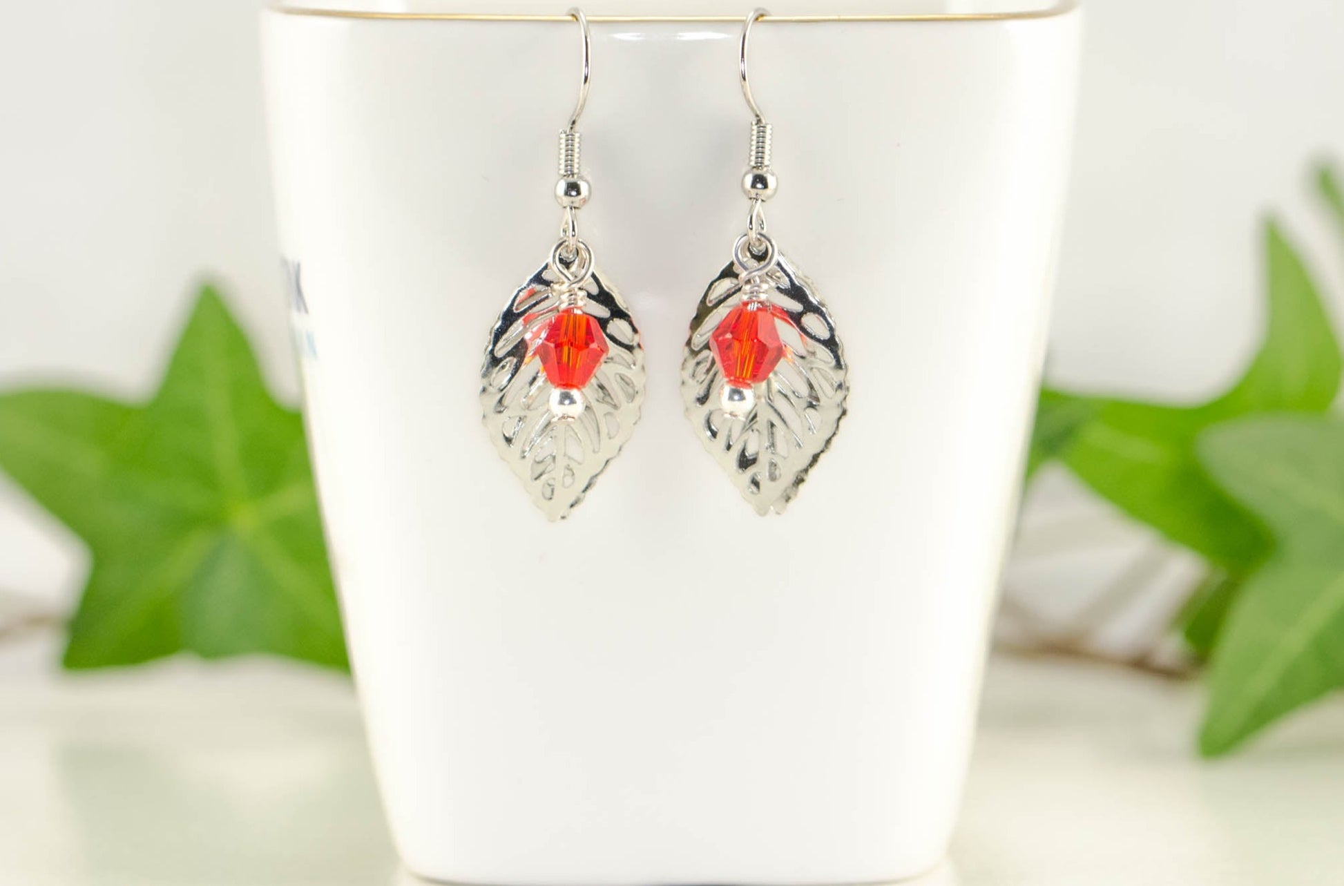 Filigree Silver Leaf Charm and Red Glass Crystal Earrings displayed on a tea cup.