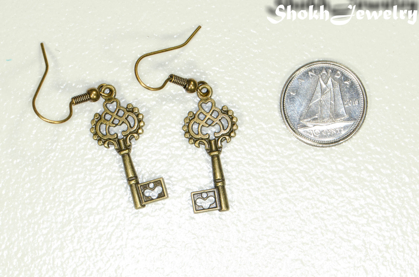 Bronze Skeleton Key Charm Earrings beside a dime.