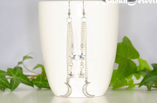 Extra Long Crescent Moon and Hematite Star Earrings displayed on a coffee mug.