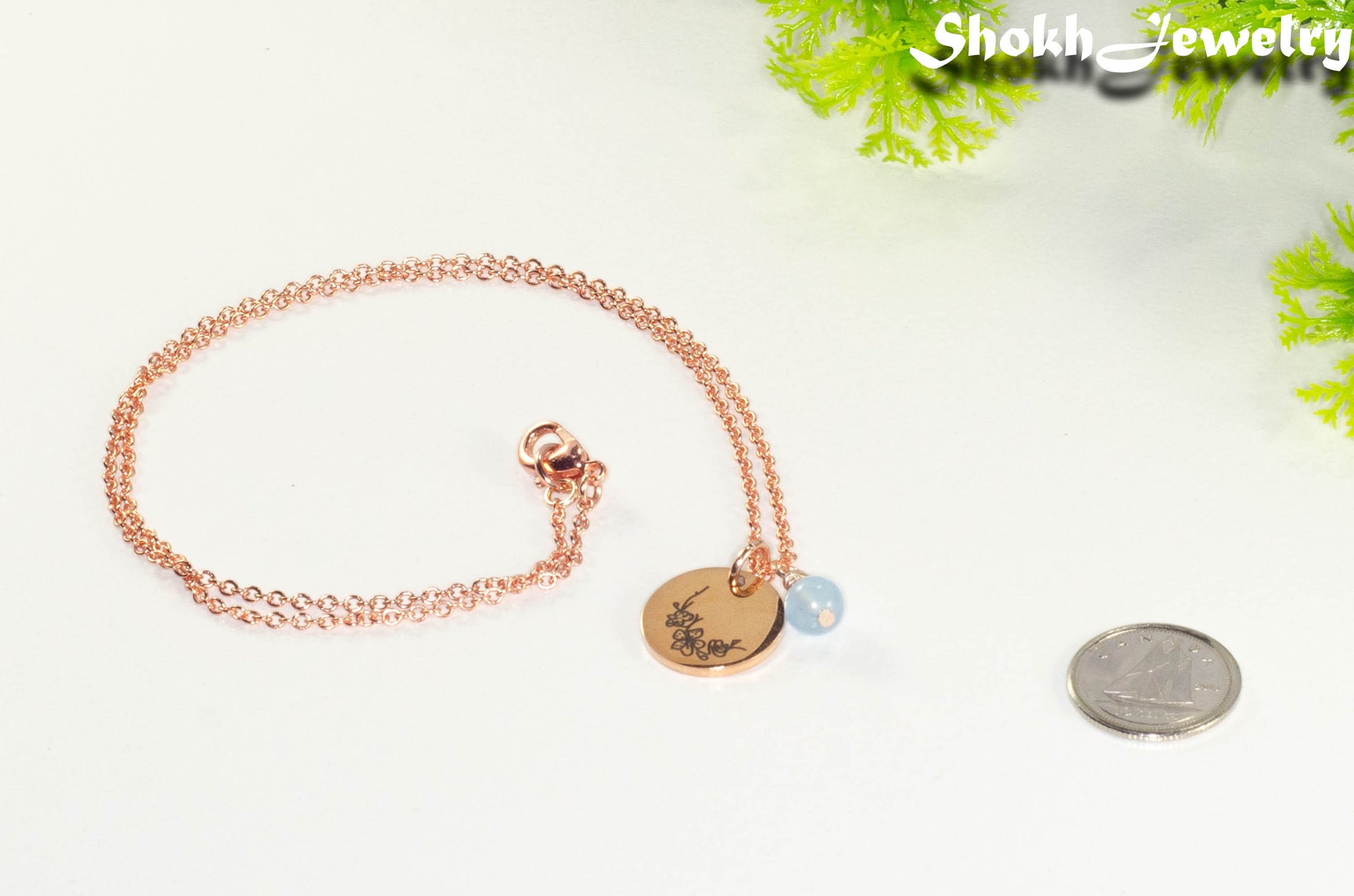 Rose Gold Plated March Birth Flower Necklace with Aquamarine Birthstone Pendant beside a dime.