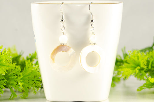 White Doughnut Seashell Earrings displayed on a tea cup.