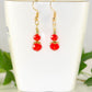 Small Red Glass Bead Dangle Earrings displayed on a tea cup.