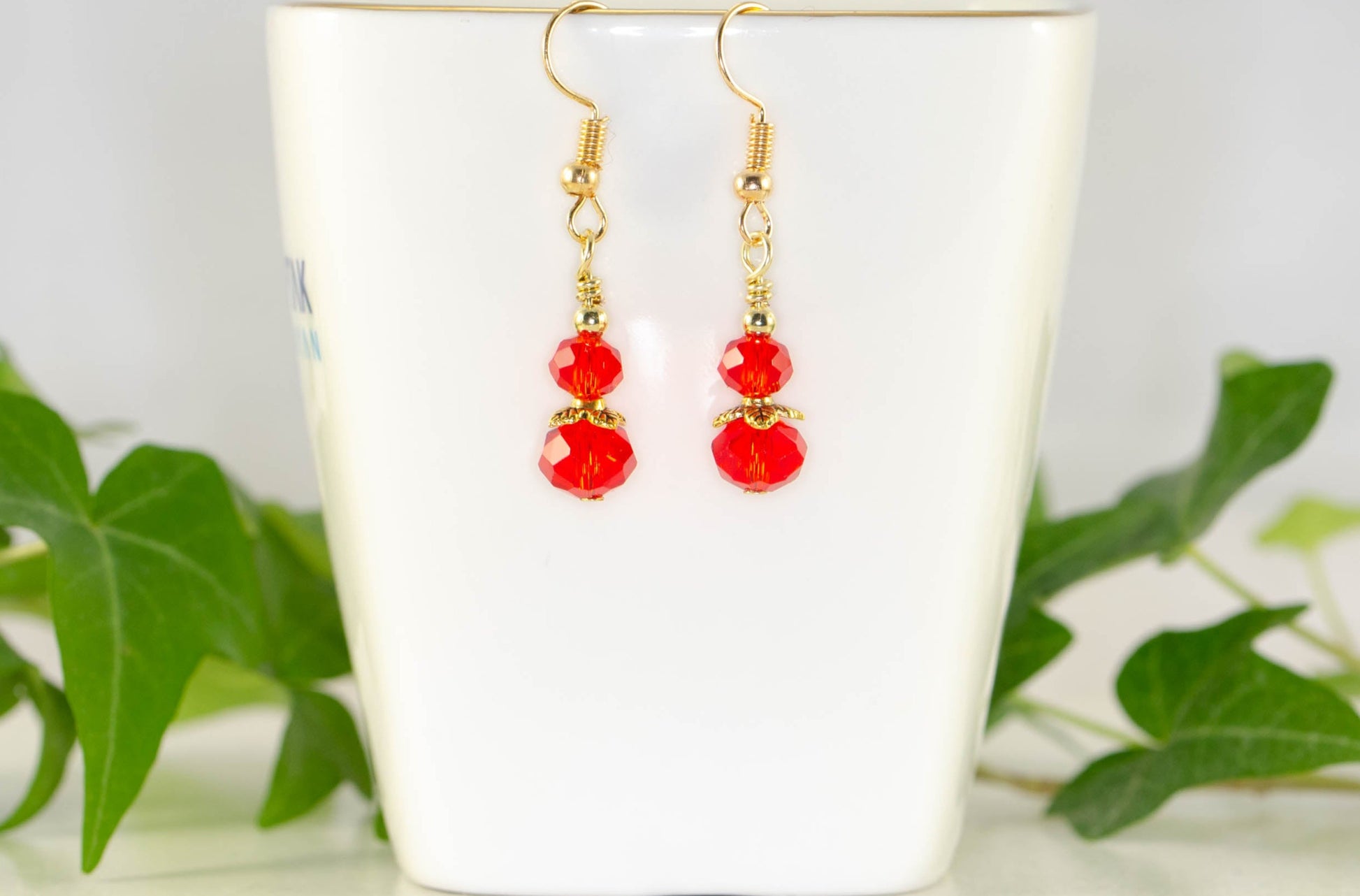 Small Red Glass Bead Dangle Earrings displayed on a tea cup.