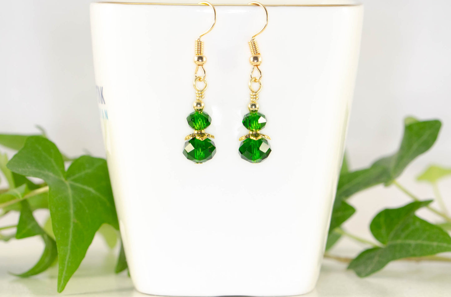 Small Dark Green Glass Bead Dangle Earrings displayed on a tea cup.