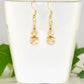 Small Light Pink Glass Bead Dangle Earrings displayed on a tea cup.