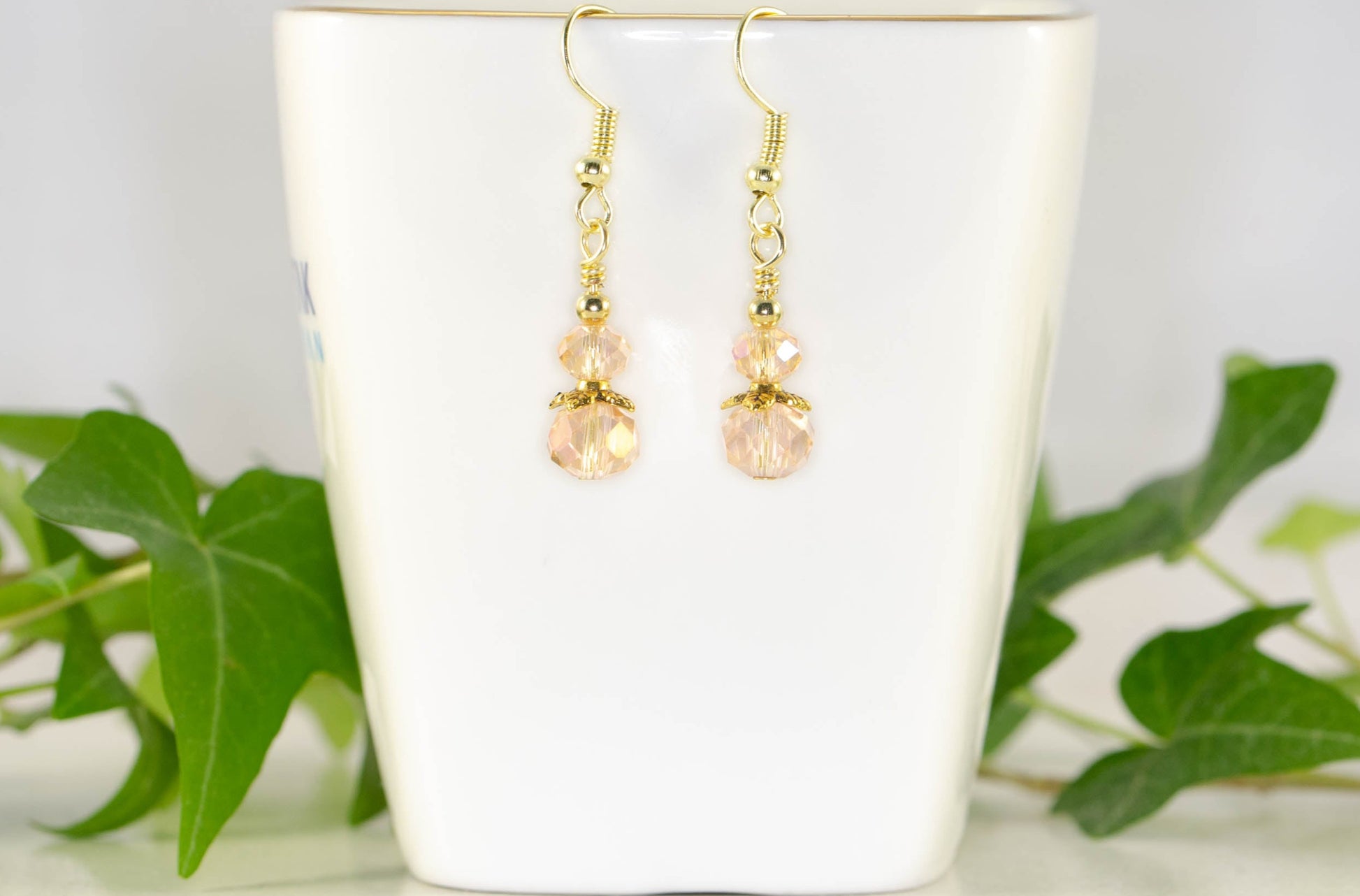 Small Light Pink Glass Bead Dangle Earrings displayed on a tea cup.