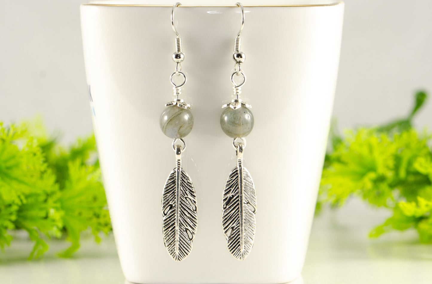 Labradorite Crystal and Tibetan Silver Feather Earrings displayed on a tea cup.