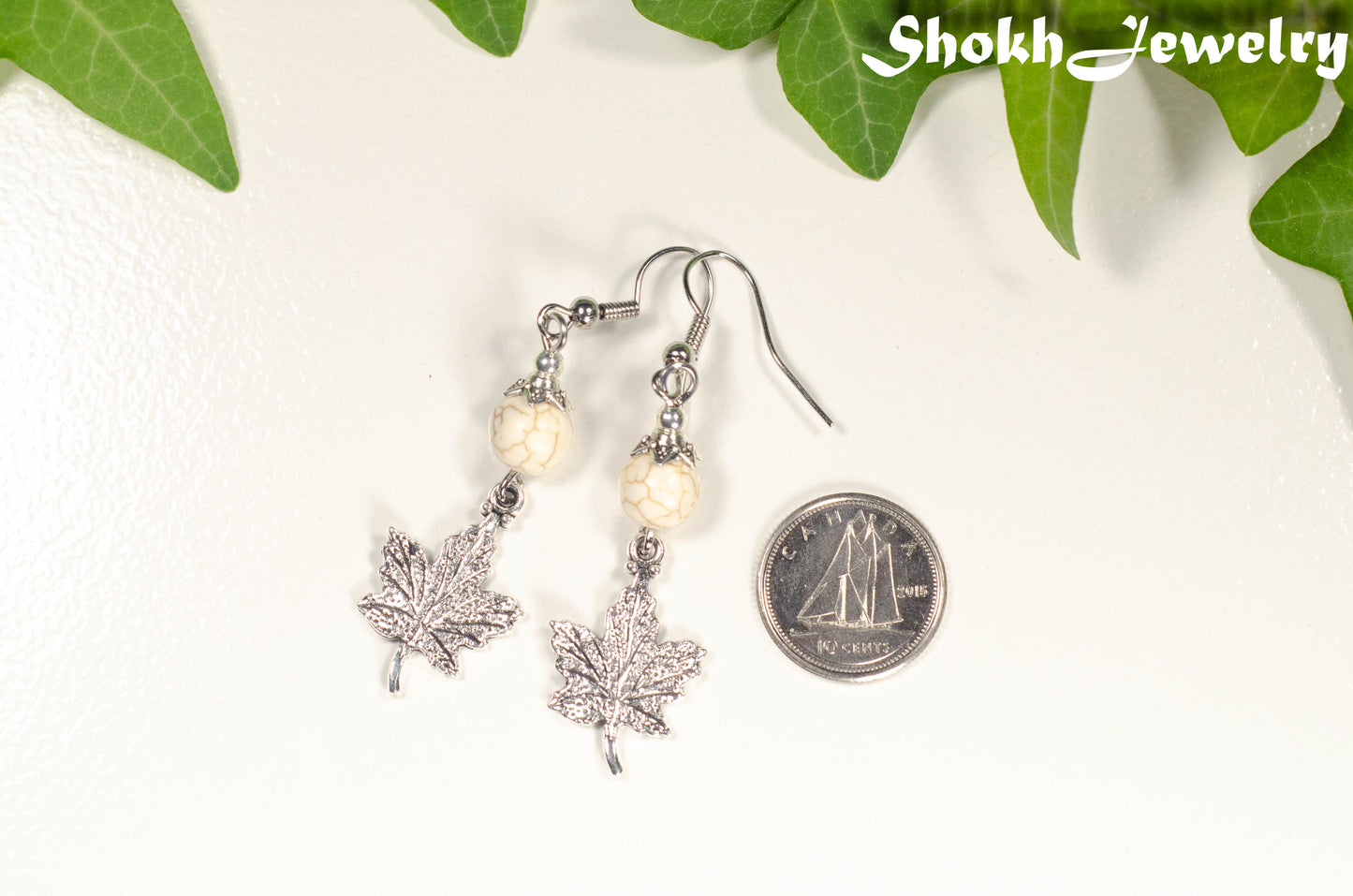White Howlite and Tibetan Silver Maple Leaf Dangle Earrings beside a dime.