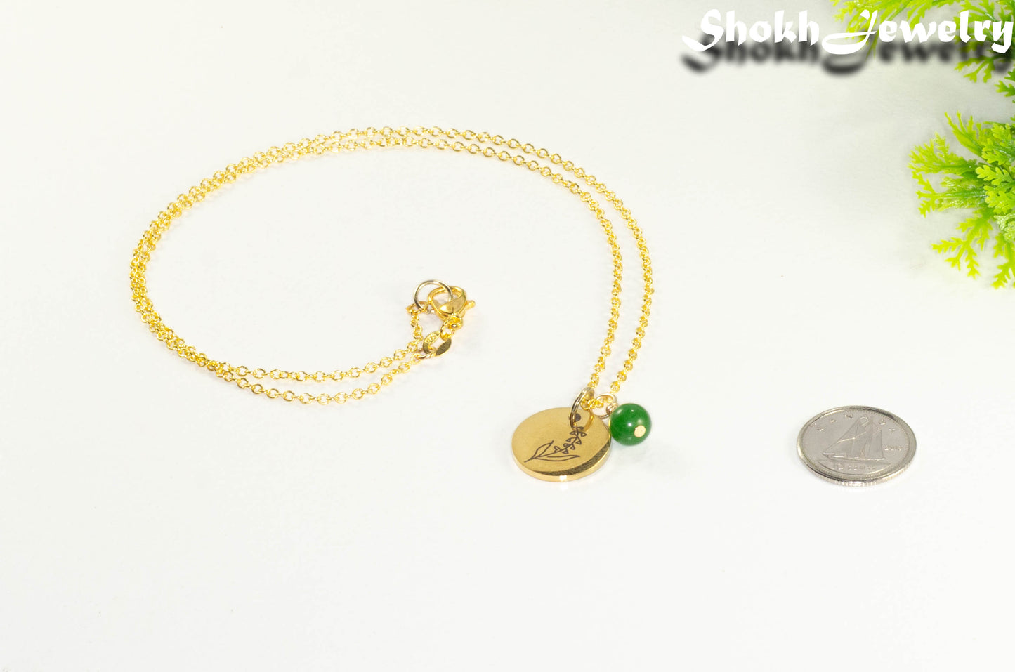 Gold Plated May Birth Flower Necklace with Emerald Birthstone Pendant beside a dime.