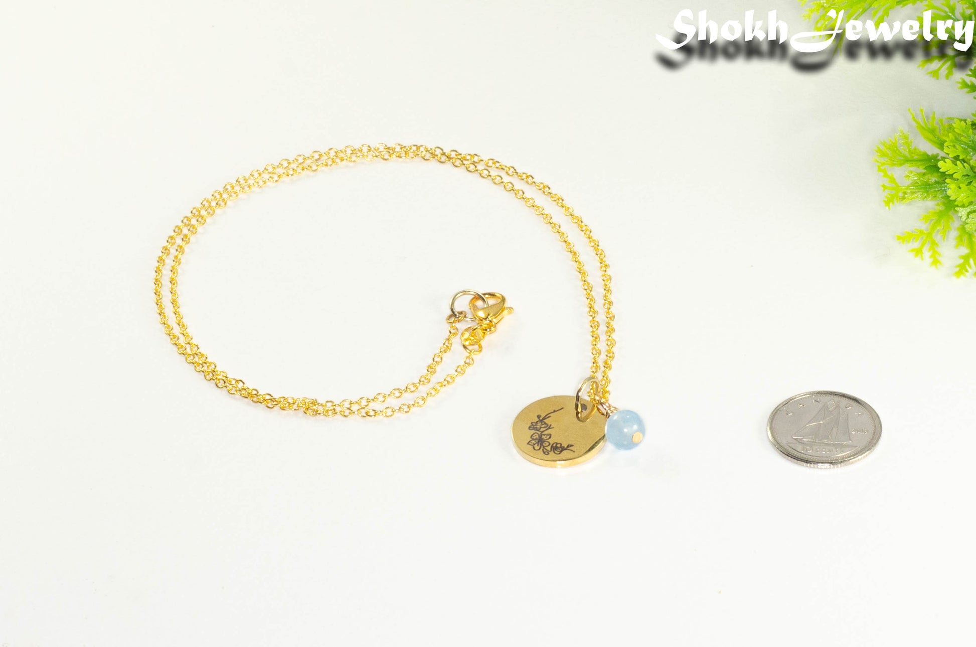 Gold Plated March Birth Flower Necklace with Aquamarine Birthstone Pendant beside a dime.