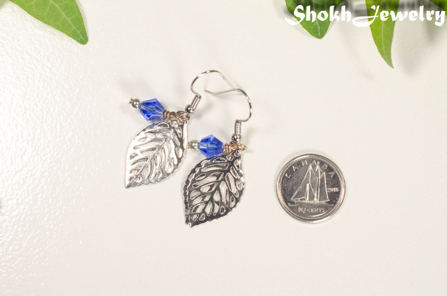 Filigree Silver Leaf Charm and Blue Glass Crystal Earrings beside a dime.