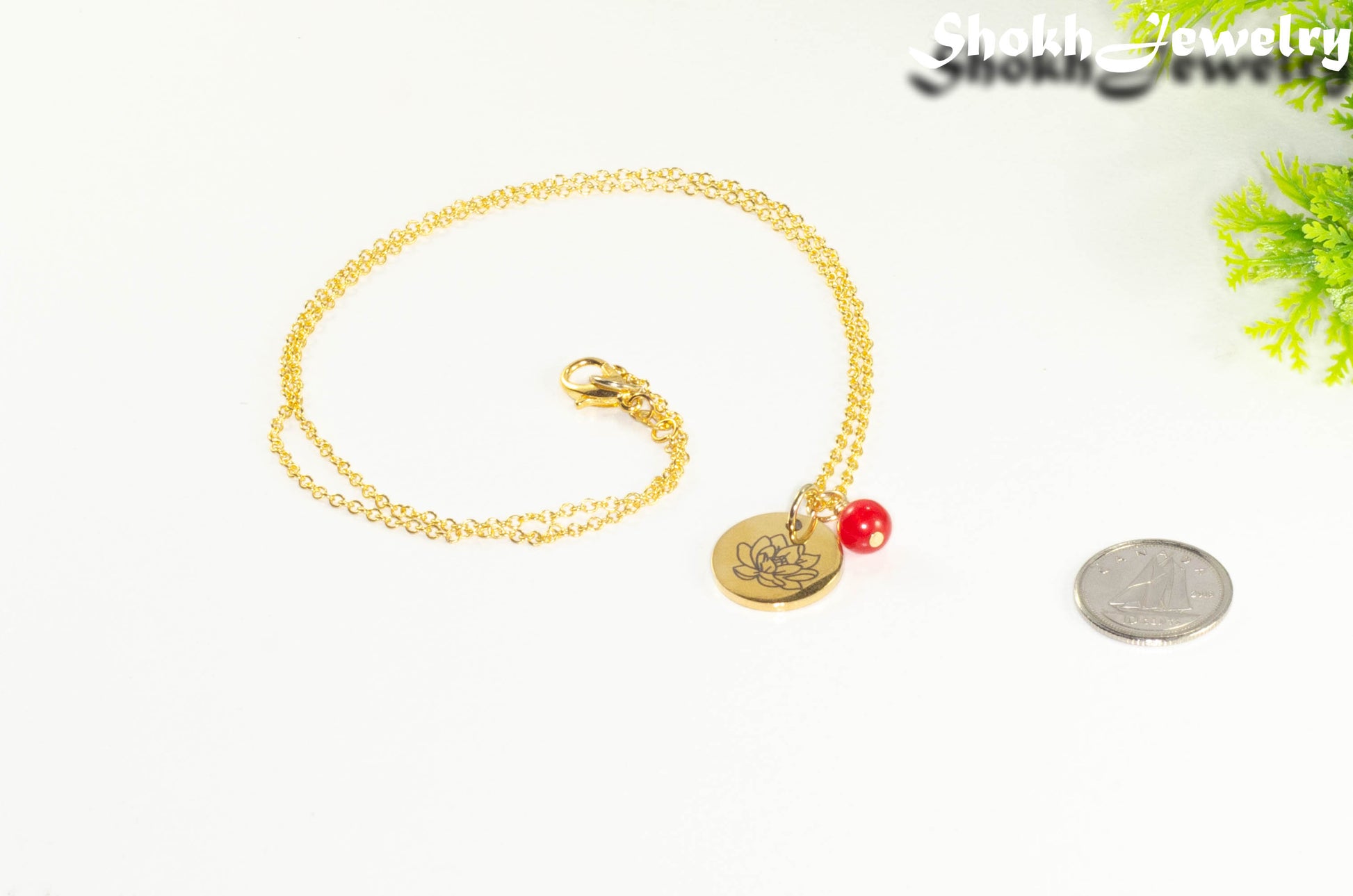 Gold Plated July Birth Flower Necklace with Red Ruby Birthstone Pendant beside a dime.