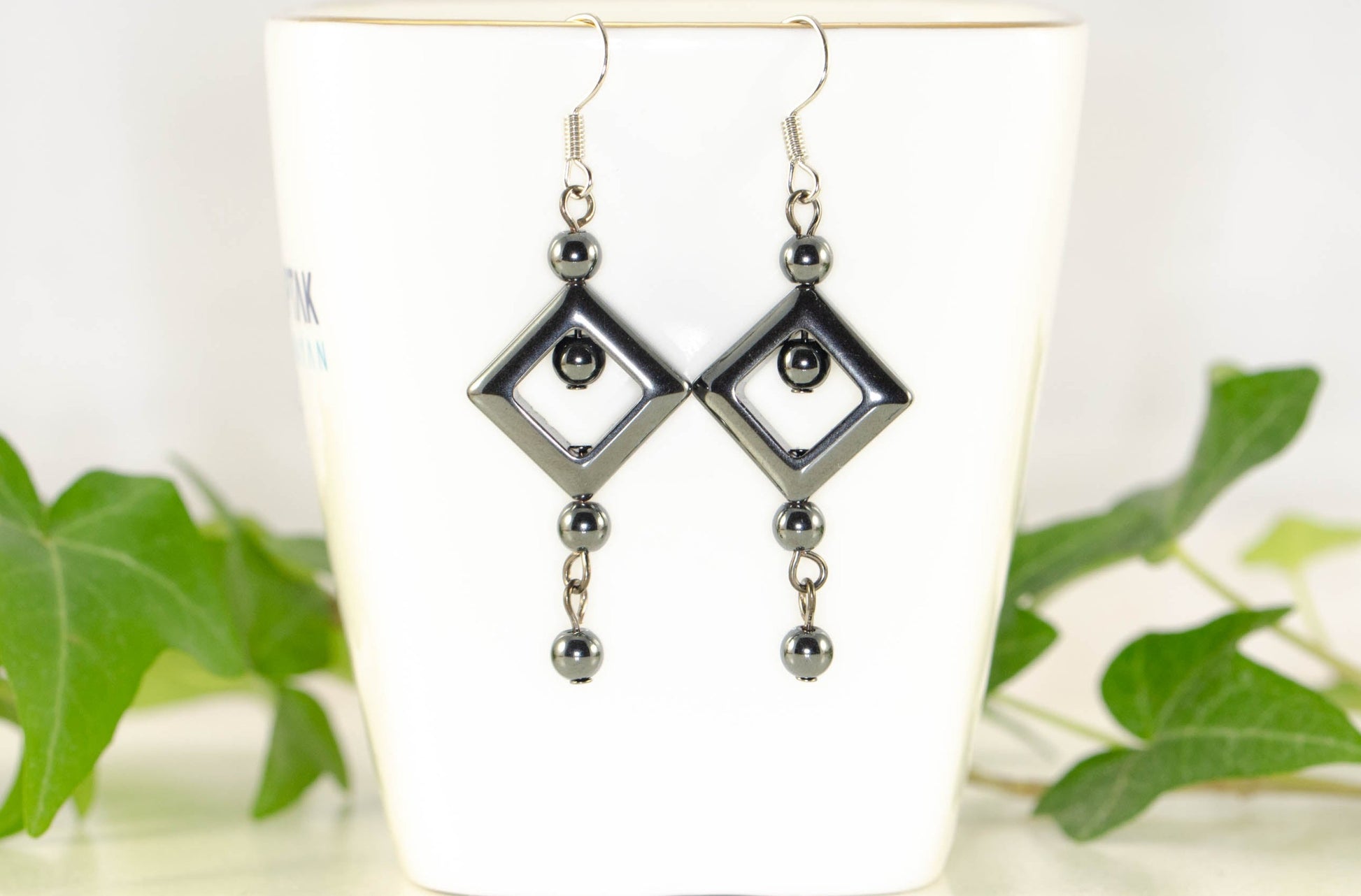 Long Black Hematite Geometric Earrings displayed on a tea cup.