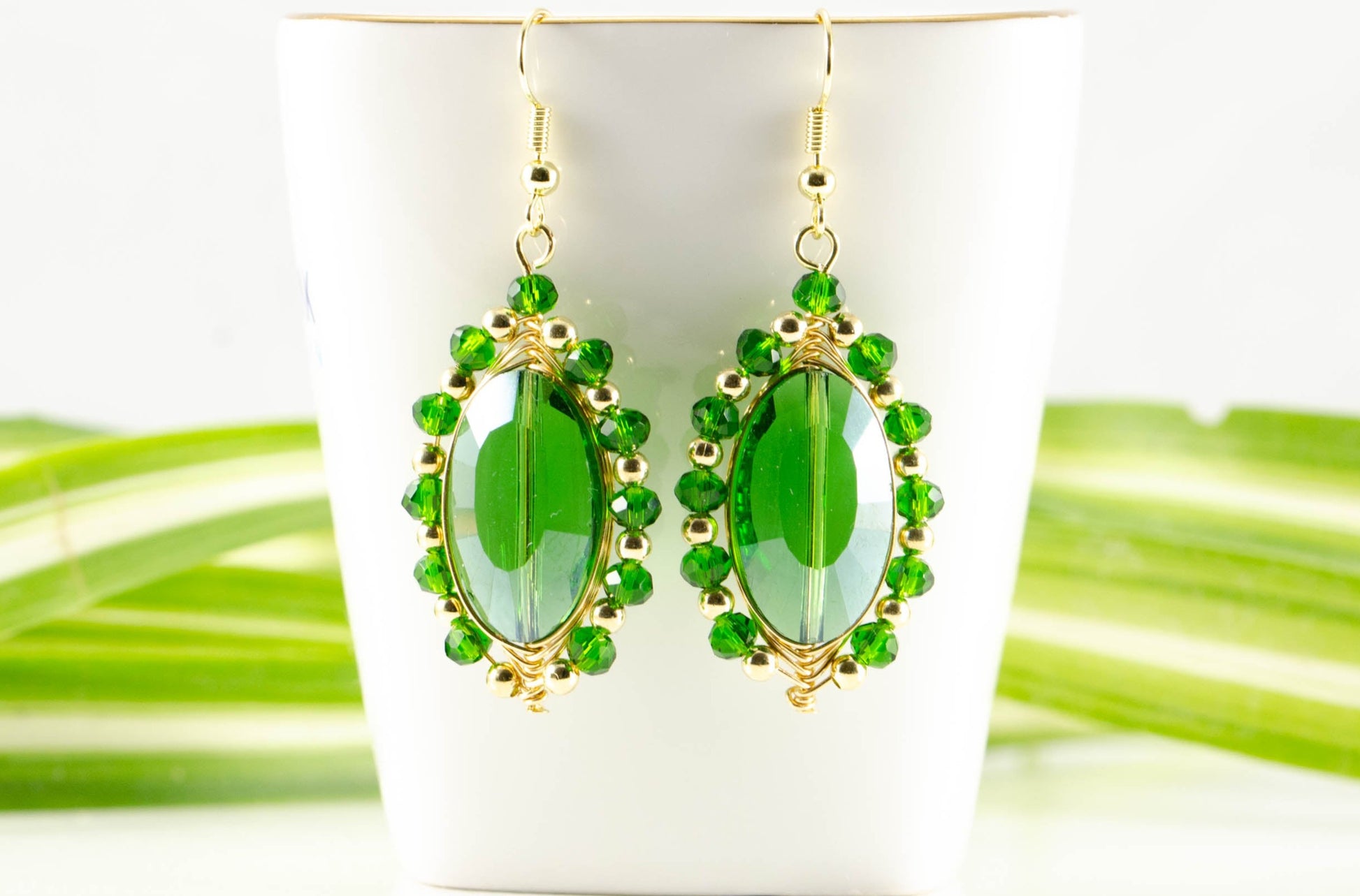 Oval Green Glass Crystal Wire Wrapped Earrings displayed on a tea cup.