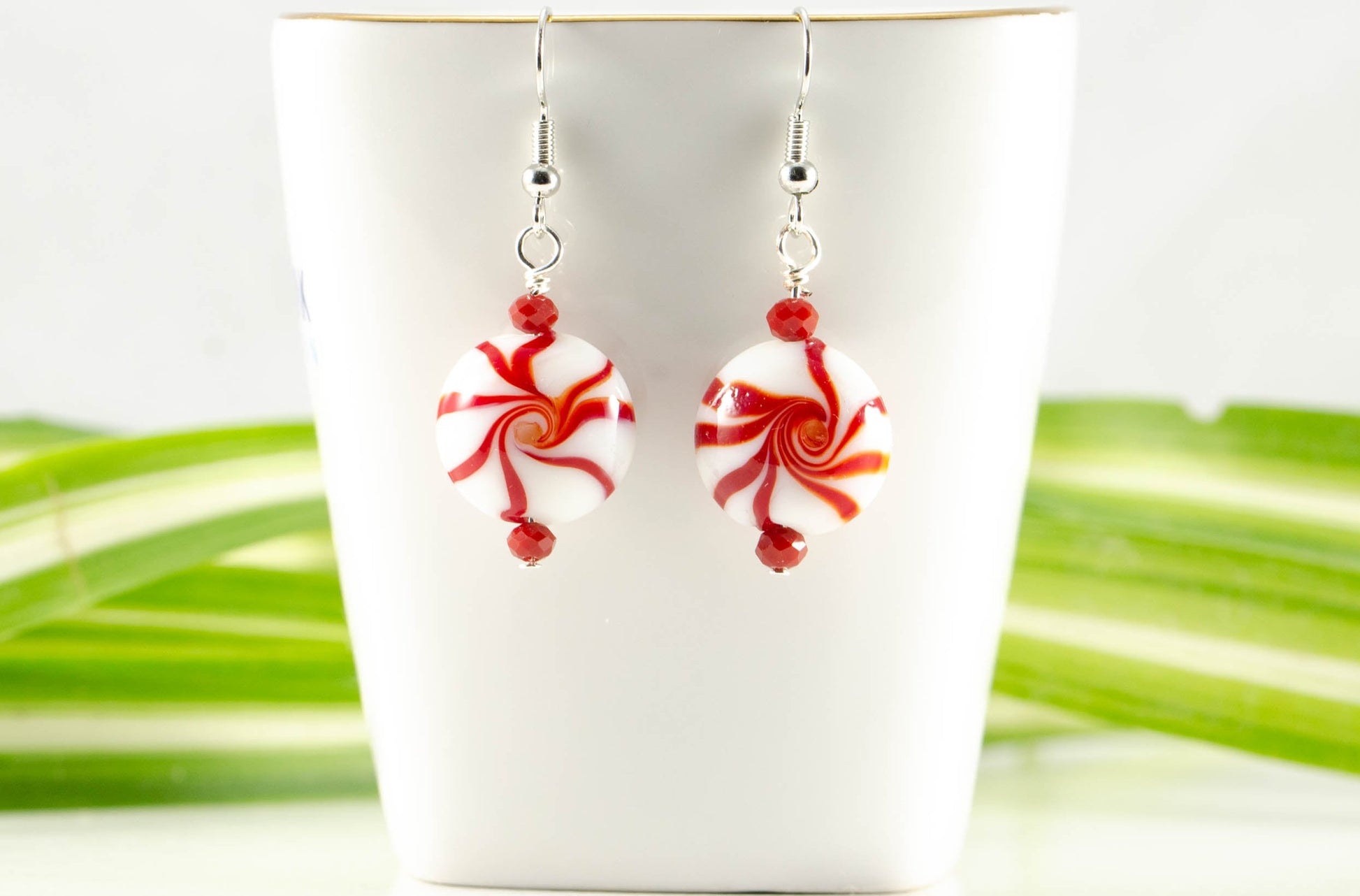 Christmas Peppermint Glass Bead Earrings displayed on a tea cup