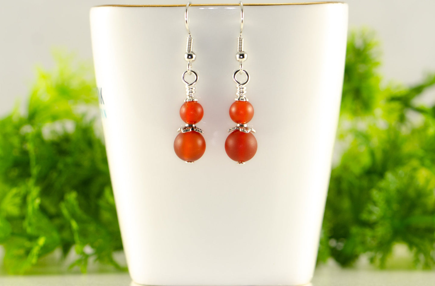 Small Matte Red Agate Earrings displayed on a tea cup.