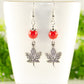 Red Howlite and Tibetan Silver Maple Leaf Dangle Earrings displayed on a tea cup.