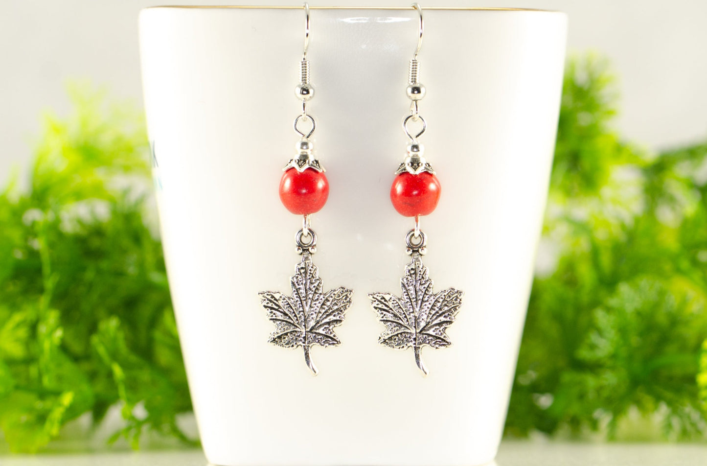 Red Howlite and Tibetan Silver Maple Leaf Dangle Earrings displayed on a tea cup.