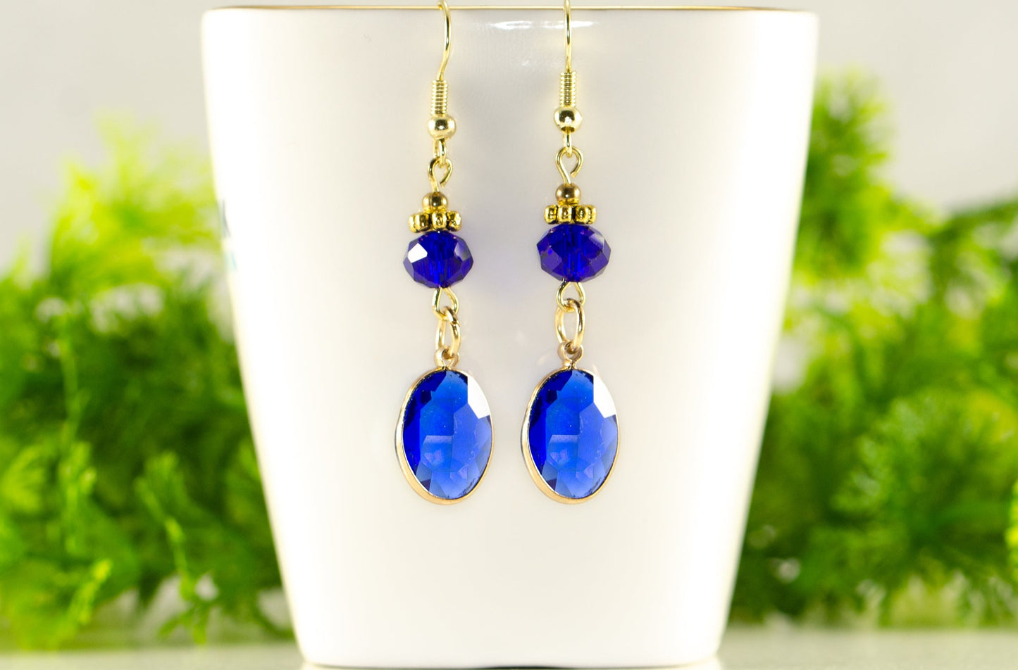 Navy Blue Oval Glass Dangle Earrings displayed on a tea cup.