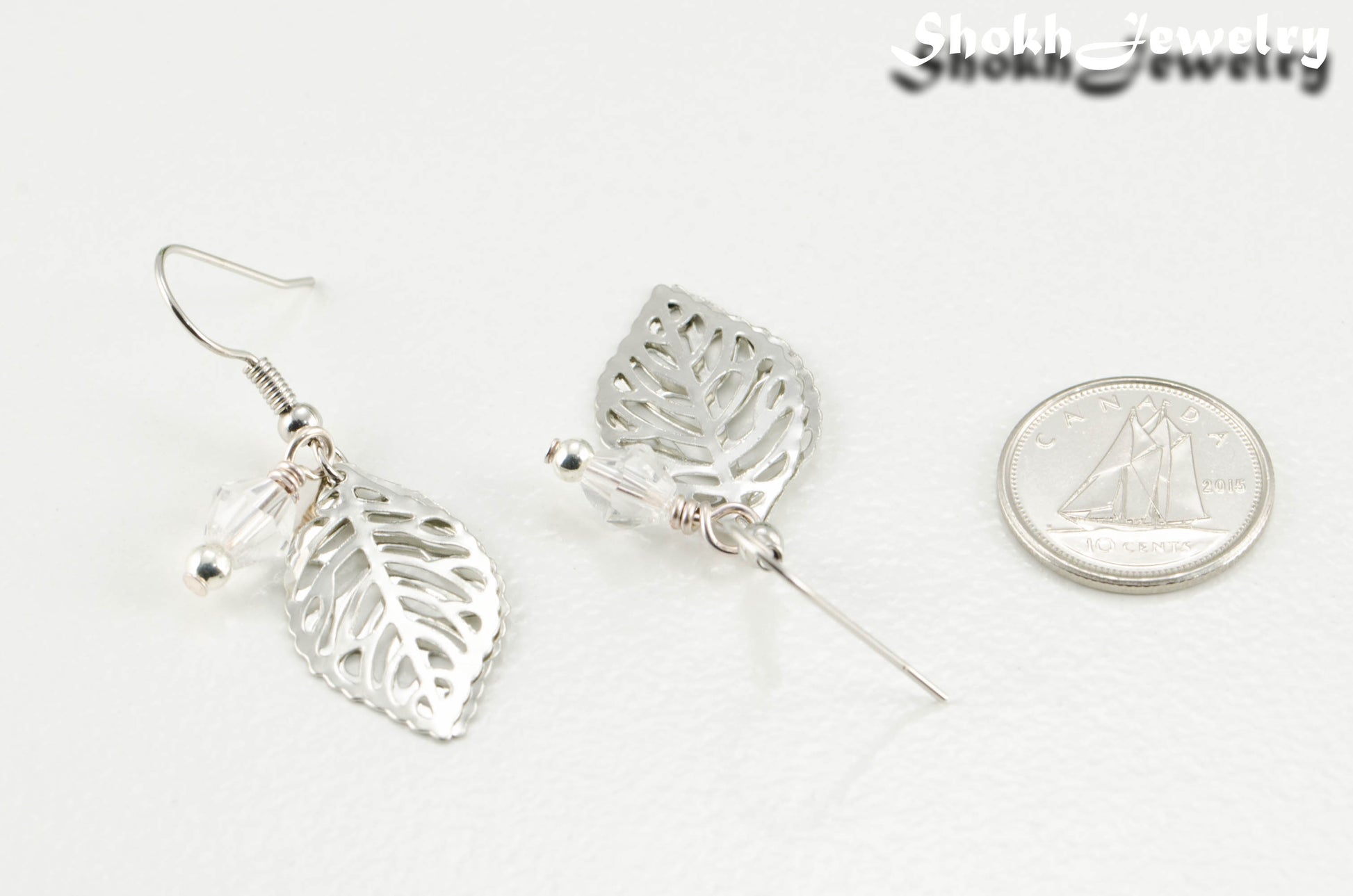 Filigree Silver Leaf Charm and Clear Glass Crystal Earrings beside a dime.