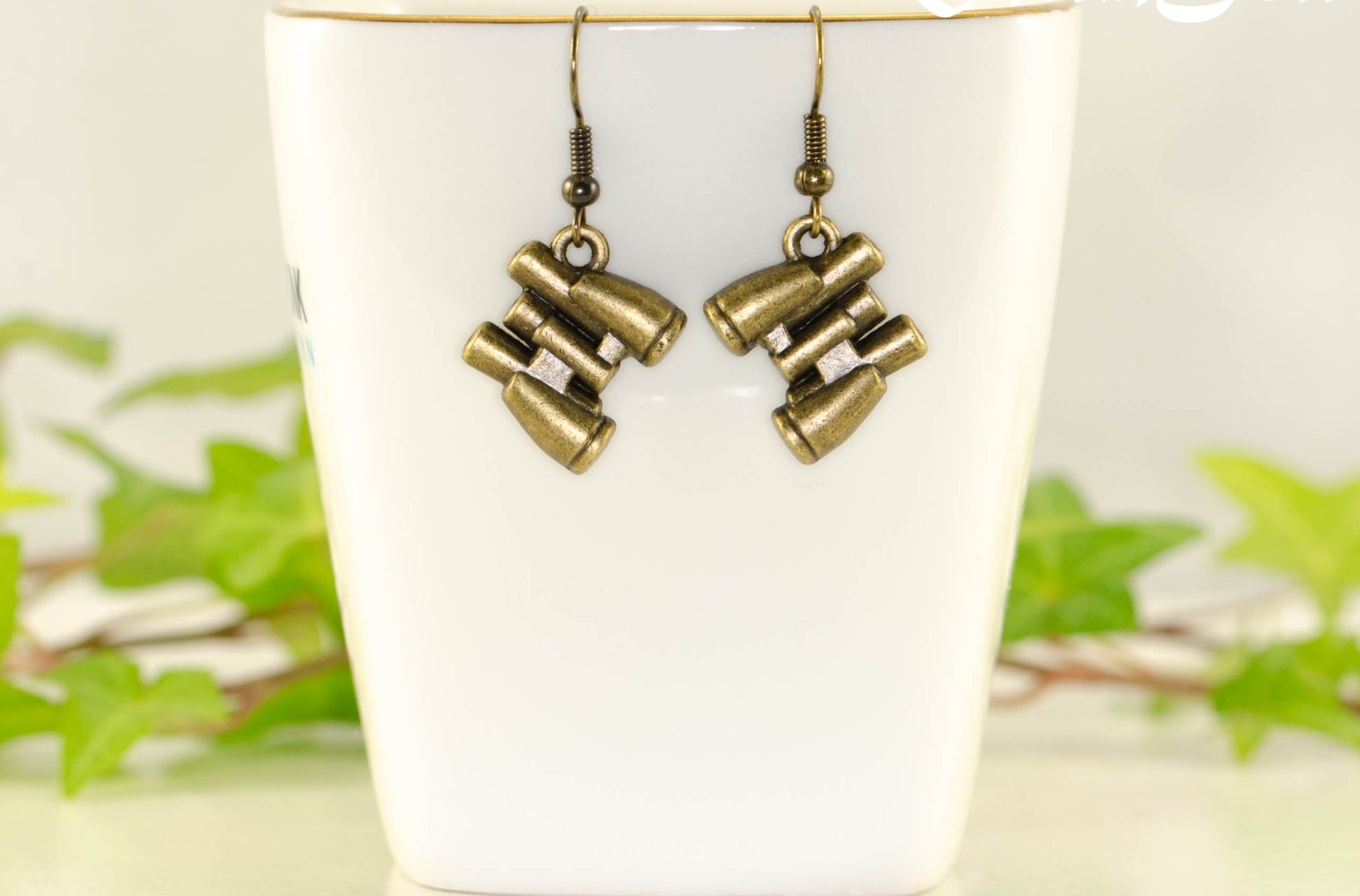 Antique Bronze Binocular Charm Earrings displayed on a tea cup.