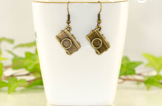 Antique Bronze Camera Charm Earrings displayed on a tea cup.