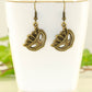 Antique Bronze Masquerade Mask Charm Earrings displayed on a tea cup.