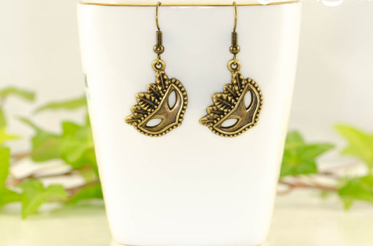 Antique Bronze Masquerade Mask Charm Earrings displayed on a tea cup.