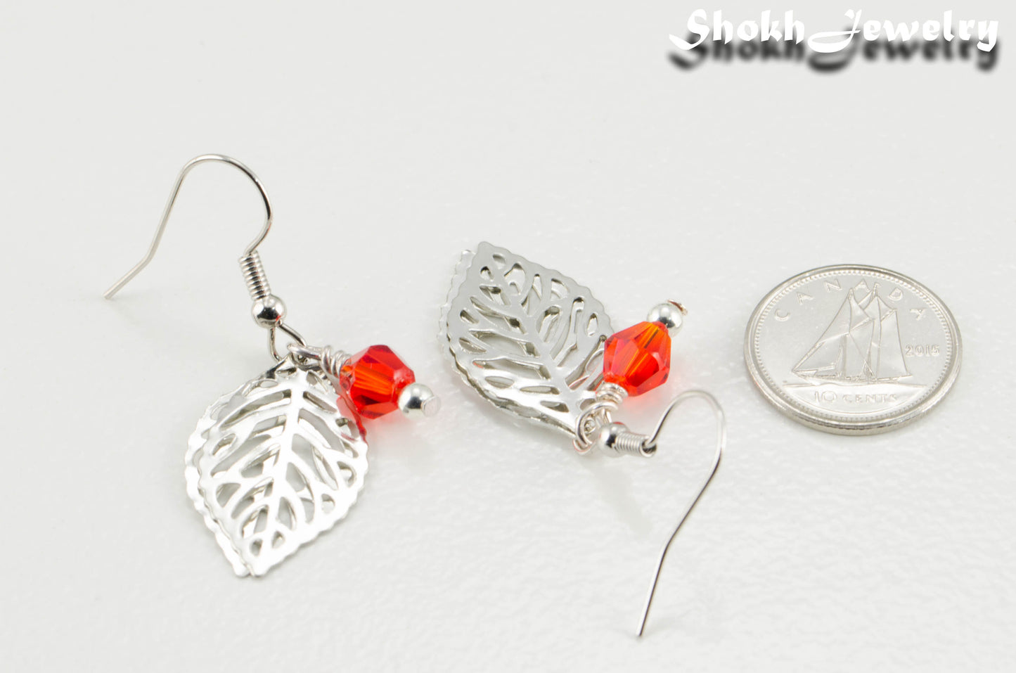 Filigree Silver Leaf Charm and Red Glass Crystal Earrings beside a dime.