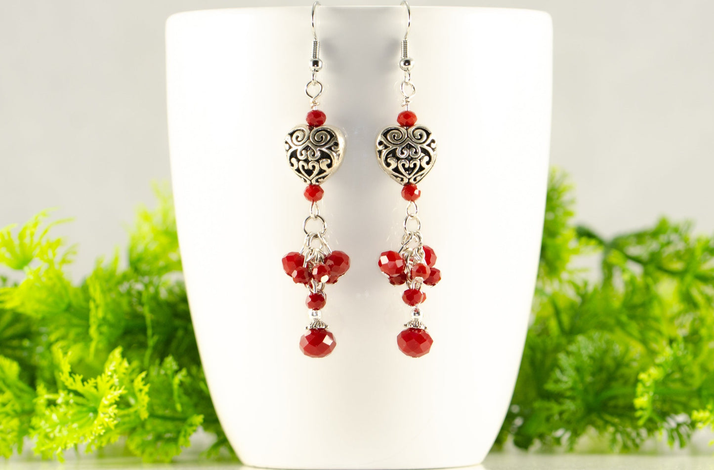 Tibetan Silver Heart and Red Beaded Cluster Earrings displayed on a coffee cup.