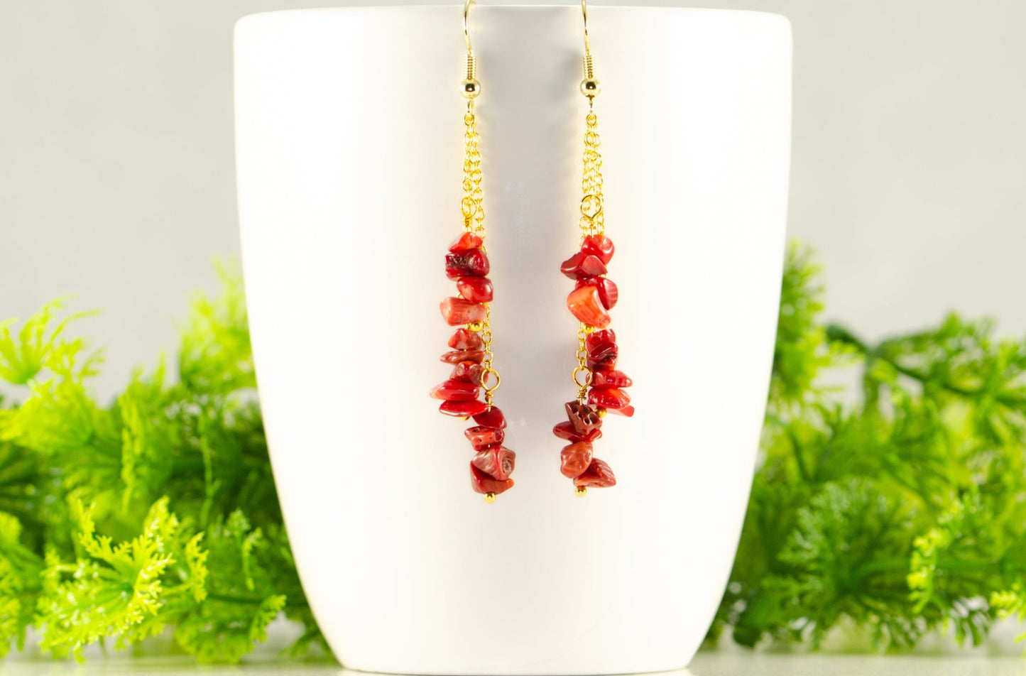 Long Gold Plated Chain and Red Dyed Bamboo Coral Chip Earrings displayed on a coffee mug.