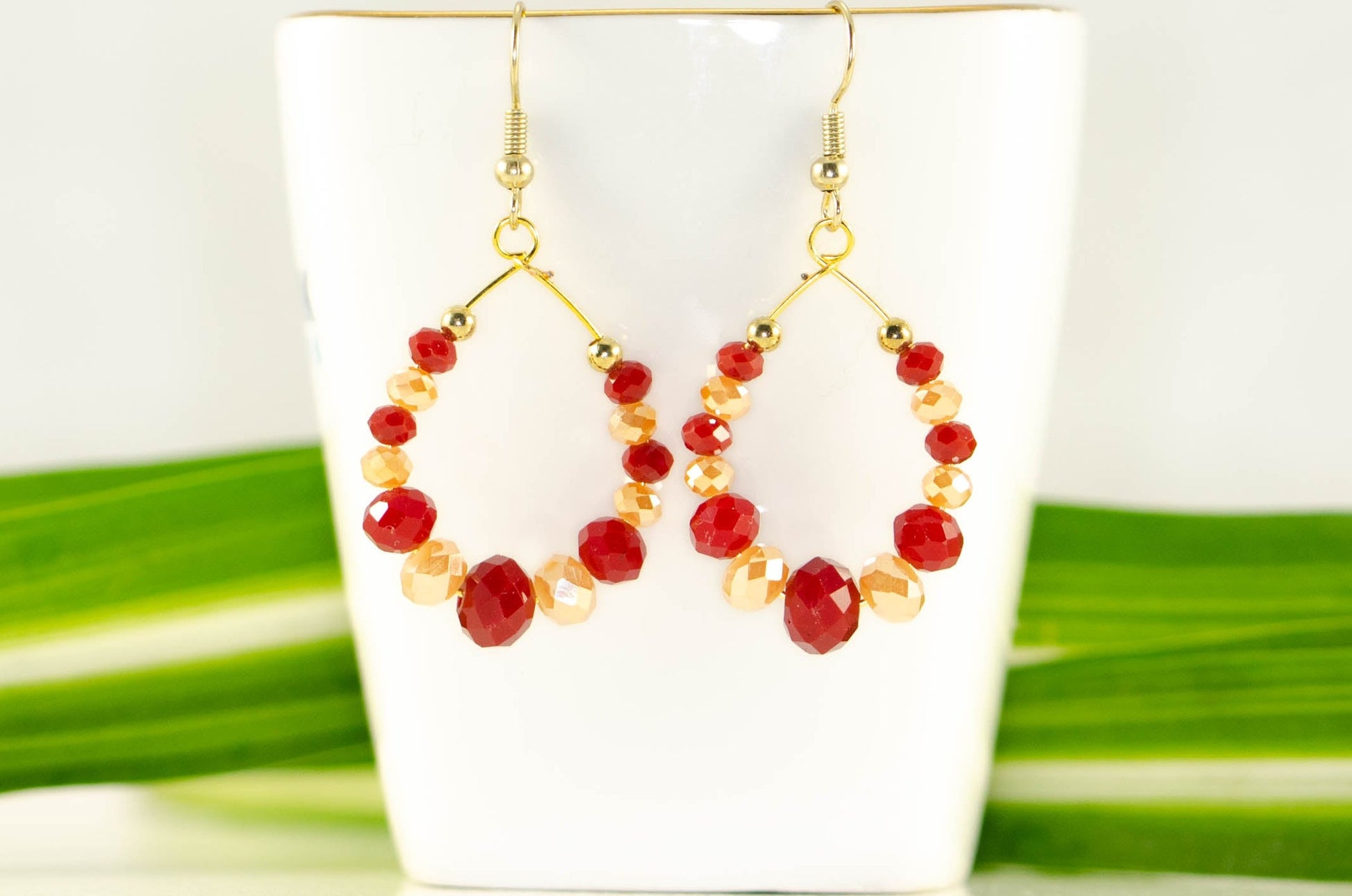 Red and Gold Glass Crystal Hoop Earrings displayed on a tea cup.