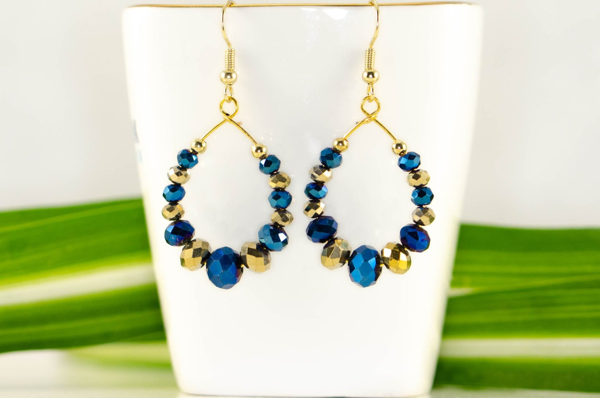 Blue and Gold Glass Crystal Hoop Earrings displayed on a tea cup.