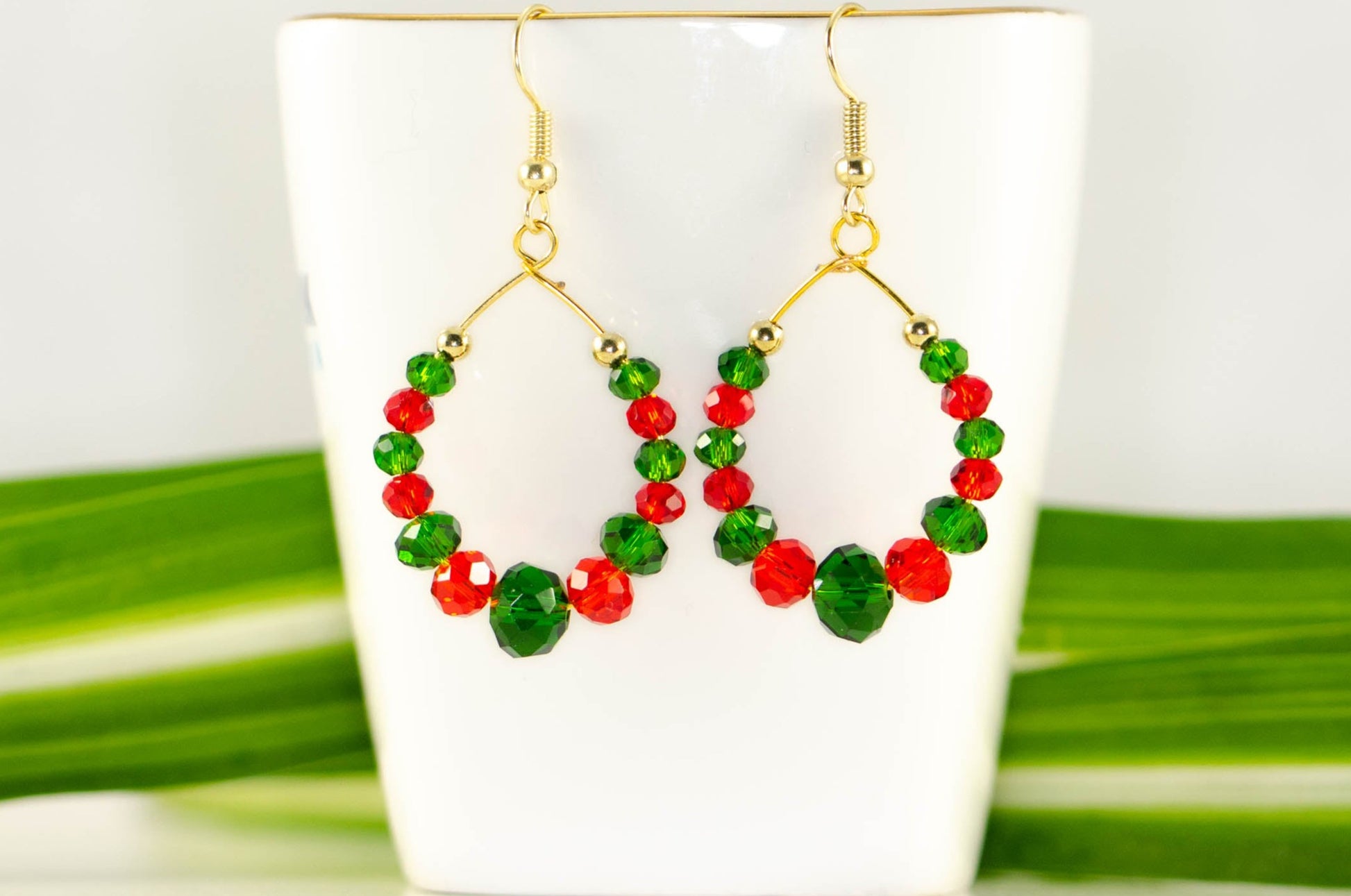 Green and Red Glass Crystal Hoop Earrings displayed on a tea cup.