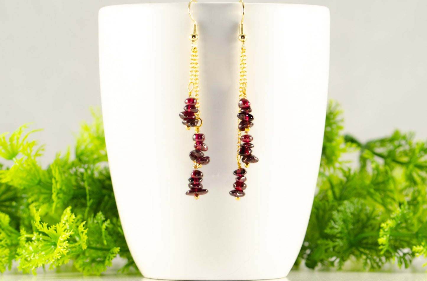 Long Gold Plated Chain and Garnet Crystal Chip Earrings displayed on a coffee mug.