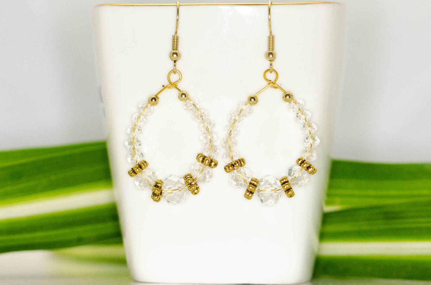 Clear Glass Crystal and Gold Hoop Earrings displayed on a tea cup.