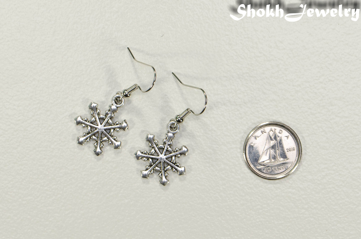 Christmas Snowflakes Charm Earrings beside a dime.