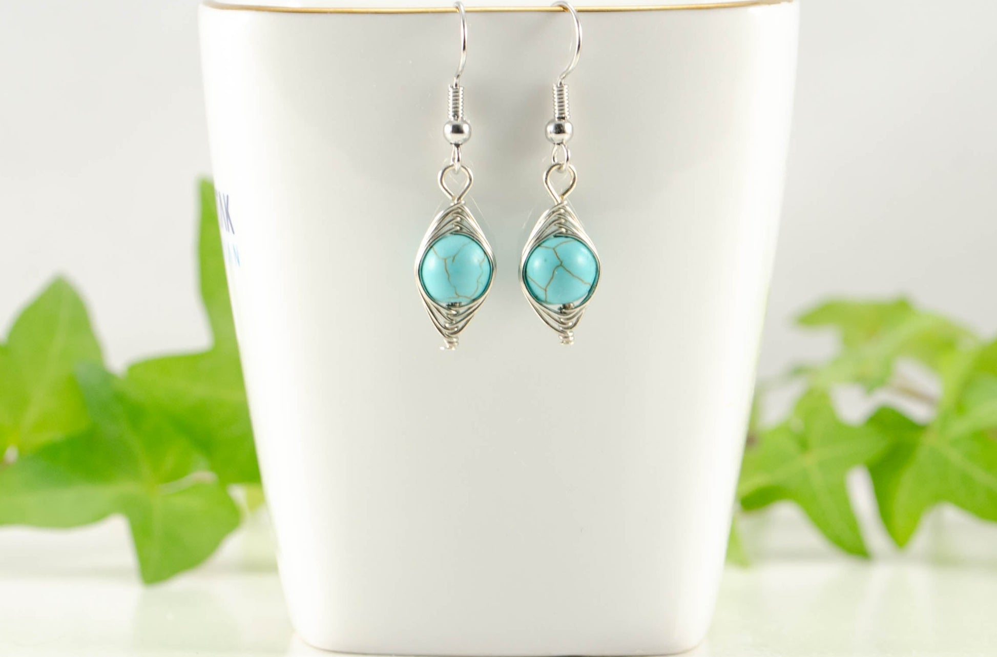 Turquoise Howlite Wire Wrapped Earrings displayed on a tea cup.