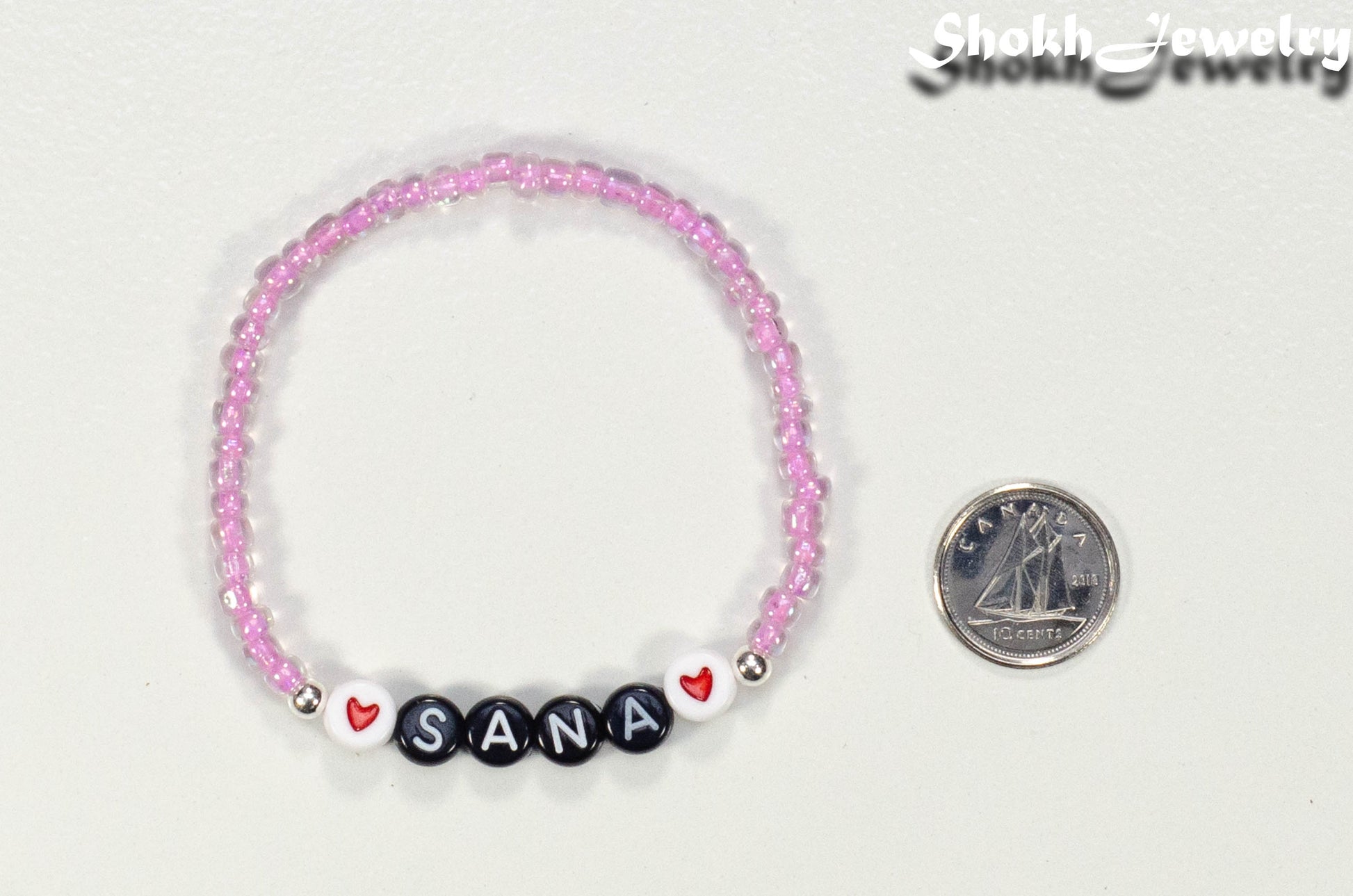 Pink Seed Beads Name Bracelet beside a dime.