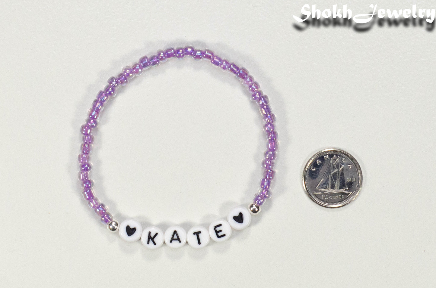 Purple Seed Beads Name Bracelet beside a dime.
