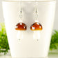 Brown Mushroom Glass Bead Earrings displayed on a tea cup.