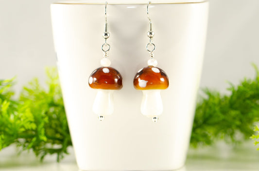 Brown Mushroom Glass Bead Earrings displayed on a tea cup.