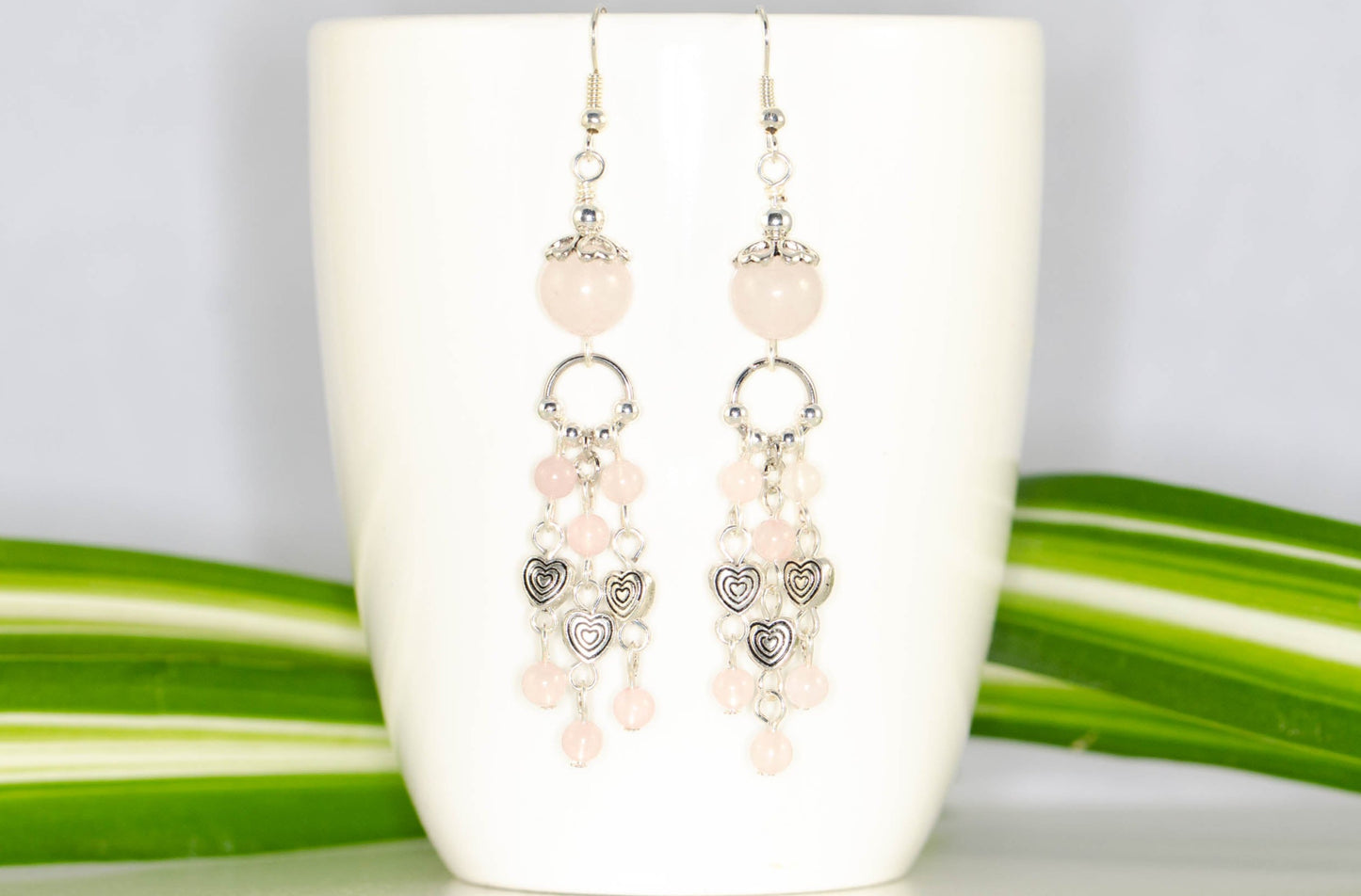 Statement Rose Quartz and Heart Chandelier Earrings displayed on a coffee mug.